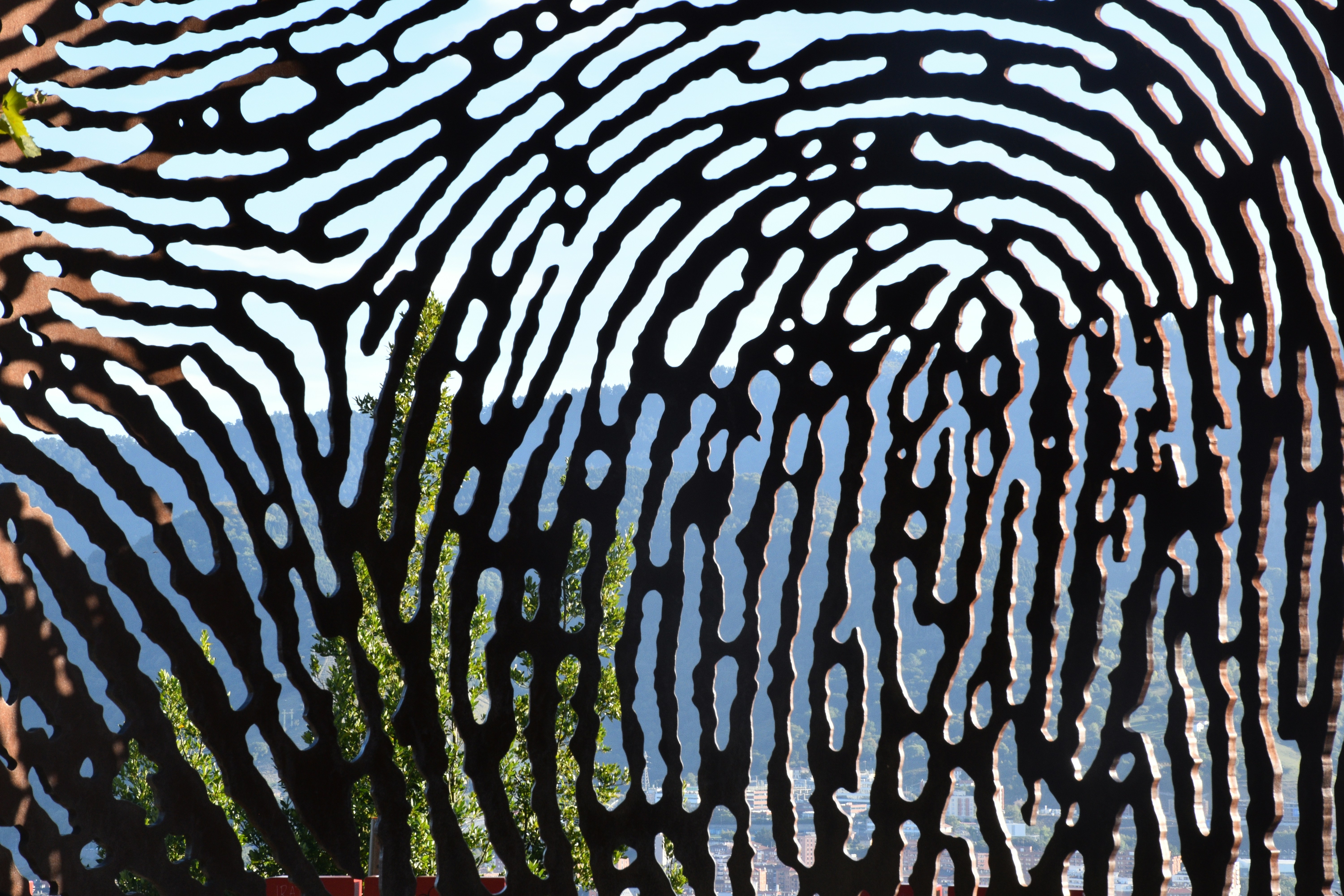 A metal screen with a fingerprint pattern framing a view of distant mountains